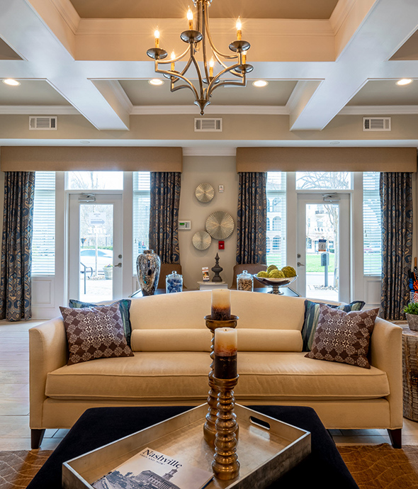 Symmetrical view of lounge with wide plush couch, coffee table with tray and large candle holders, and sculpted chandelier.